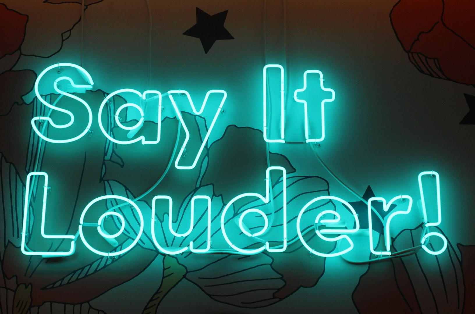 The sentence 'Say It Louder!' in large, green neon lights.